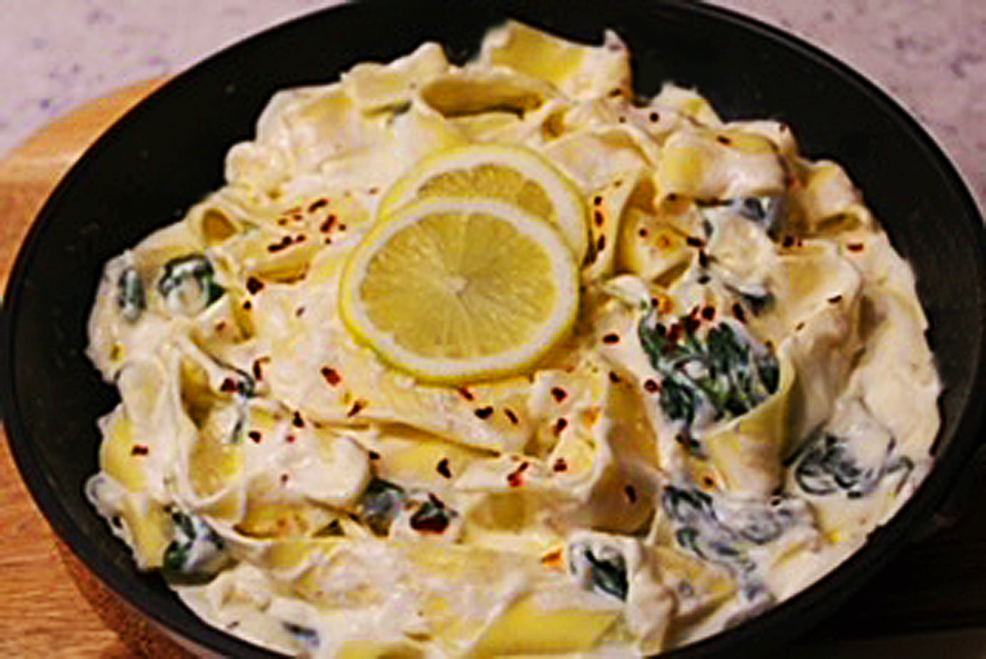 Pappardelle pasta sautéed with lemon ricotta sauce with spinach in a sauté pan w/ two lemon slices