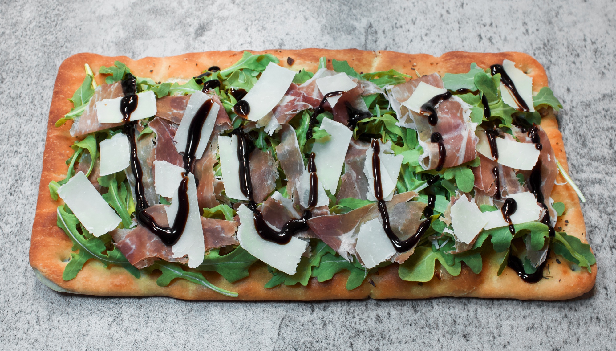 Flatbread layered with fresh arugula, slices of prosciutto, shaved Parmesan cheese & balsamic glaze 