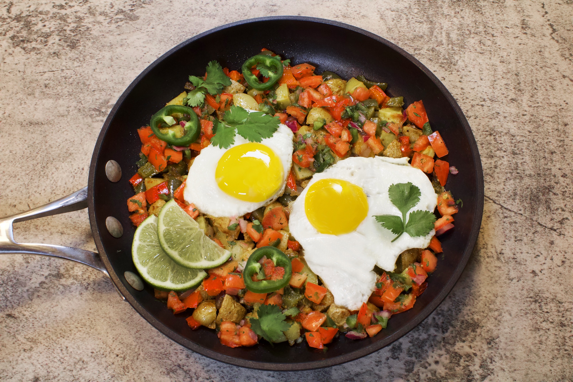 A skillet with two sunny side up eggs, over a potato pepper hash. 